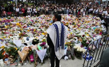 Rabbi Yossi Friedman speaks to people gathering at a flower memorial by the Bondi Pavilion at Bondi Beach on Tuesday, Dec. 16, 2025, following Sunday's shooting in Sydney, Australia. (AP Photo/Mark Baker)